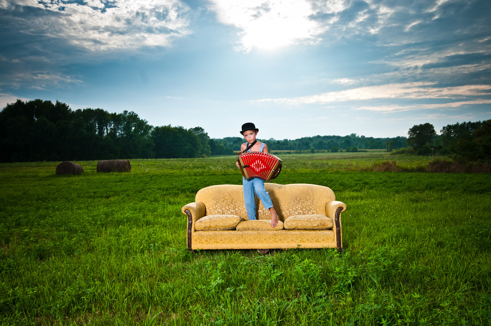 portrait of young boy playing accordion on a vintage sofa in a field